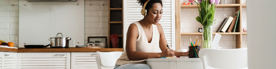 Black woman in headphones working with laptop while sitting at table