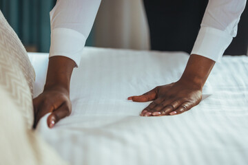 Housekeeper cleaning a hotel room. African housekeeper in a hotel room. Maid making bed in hotel room. Staff Maid Making Bed.  African housekeeper making bed.