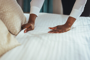 Fototapeta premium African maid making bed in hotel room. Staff Maid Making Bed. African housekeeper making bed. Maid working at a hotel making the bed. Housekeeper cleaning a hotel room