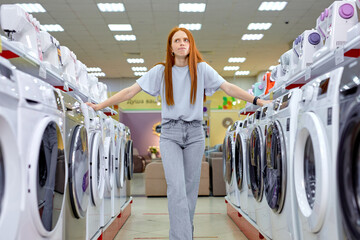 Hard decision.Beautiful lady choosing between two washing machines, female standing by new washing...