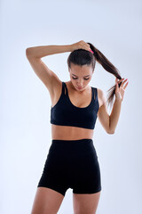 Fototapeta na wymiar portrait of slim fitness woman making ponytail preparing for sport workout, wearing bblack tracksuit short top and shorts. brunette lady is looking down confidently. sport and fitness concept