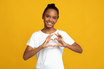 Happy teen african american girl pupil blogger in white t-shirt show heart gesture with hands