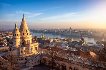 The main tower of the impressive Fisherman's Bastion (Halaszbastya) from above with Hungarian Parliament building and River Danube at background during a golden sunrise in Budapest - obrazy, fototapety, plakaty