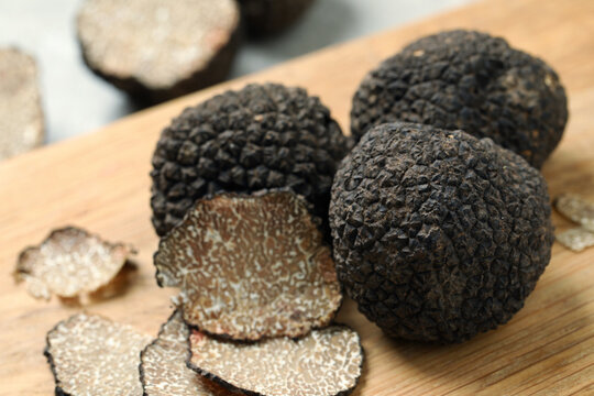 Whole and cut black truffles on wooden board, closeup