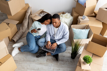 Moving, relocating concept. Loving african american couple purchasing furniture for new apartment, using laptop