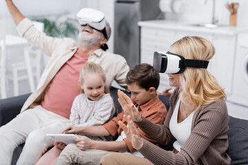 excited couple gaming in vr headsets near grandchildren using digital tablet on couch. - Powered by Adobe