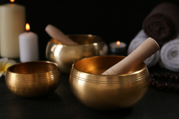 Golden singing bowls with mallets on black table against dark background