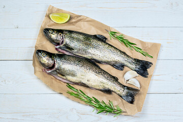 Raw fish, trout with pepper, garlics, lemon and rosemary on craft paper on white wooden table. Healthy food and dieting concept flat lay, top view image with copy space.