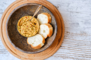 Bread baguette with homemade hummus in an old clay plate on a wooden table. A plant-based, healthy, vitamin-rich, balanced vegan food. Dish with red onion, pepper, dill and olive oil. Middle East.