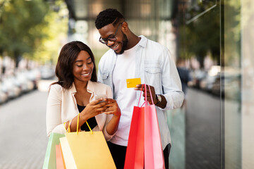 Portrait of happy afro couple using smartphone holding credit card
