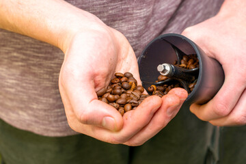 a man grinds coffee in a manual coffee grinder to pour coffee beans into a coffee grinder close-up