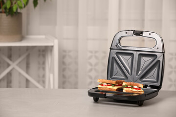 Modern grill maker with sandwiches on light grey table indoors, space for text - obrazy, fototapety, plakaty