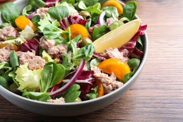 Bowl of delicious salad with canned tuna and vegetables on wooden table, closeup