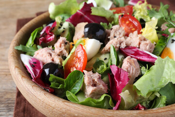 Bowl of delicious salad with canned tuna and vegetables on wooden table, closeup