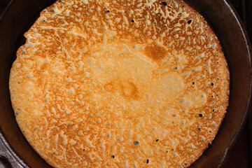 Hot fried pancake in a frying pan, close-up, top view.