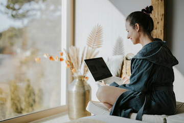 Frau im Bademantel sitzt gemütlich mit Laptop auf einem Liegestuhl