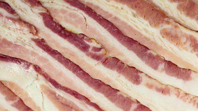 Closeup of slices of raw bacon rotating.