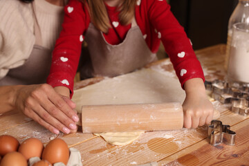 Mother and her daughter making delicious Christmas cookies at wooden table, closeup