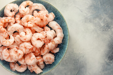Close up frozen pilled shrimps with ice cubes on a blue plate on a blurred blue background with...