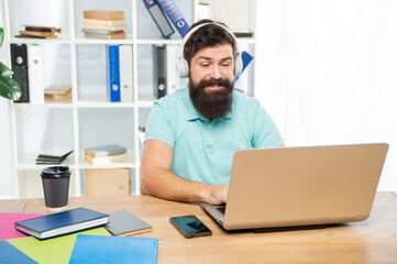 Happy businessman in headphones typing on laptop in office, online communication