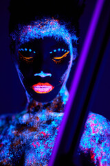 young and beautiful sensual female of black appearance in fluorescent paint makeup, posing at camera. luminescence paint, body art, neon lights. isolated on dark background