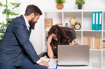 Serious office manager working while boss sitting on office desk, professionals