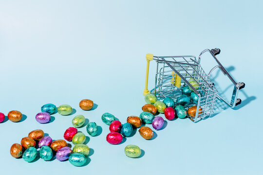 An overturned shopping cart on the ground and spilling colourful Easter eggs on a blue background.