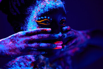 close-up black female with fluorescent prints on skin, cosmic paint glowing on neon lights, black background in studio. female with body art closing half of face, touching. beauty, fashion concept