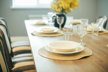 Wooden table with empty plates and glasses. Festive Easter table setting. Branches of mimosa in vase