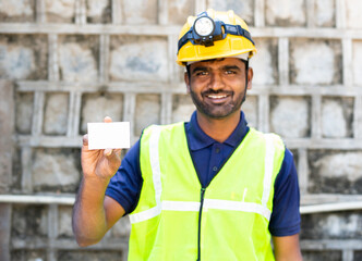 Happy smiling young electrician or repairman showing white job card by looking at camera - conncept of repair service, advertisment and promotion.