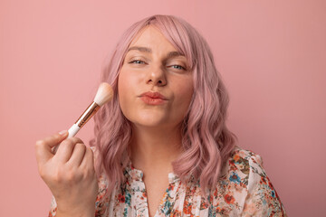 Close up portrait of happy woman smiles hold professional makeup brush apply powder isolated over pink background