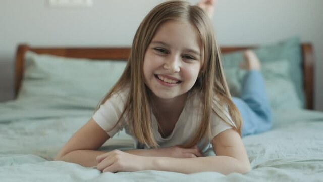Pretty girl child lying in bed, looking at camera and smiling closeup portrait. Cute female kid in bedroom