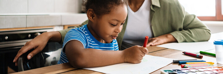 Obraz premium Black smiling woman drawing with her daughter at home kitchen