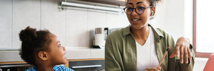Black woman working with laptop while sitting at table with her daughter
