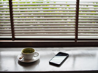 hot green tea and smartphone next to windown relaxing and rest time