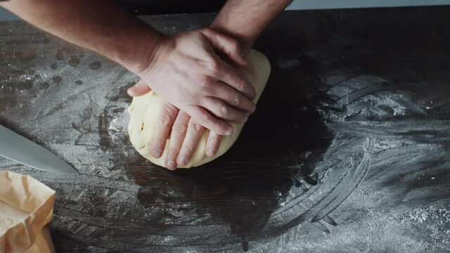 Close up shot of male chef kneading dough on wooden kitchen table covered with flour