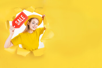 Banner of blond trendy shopaholic woman excited about new purchases holding red paper sale label in torn hole of yellow background. Happy customer is ready for online shopping. Black friday concept.