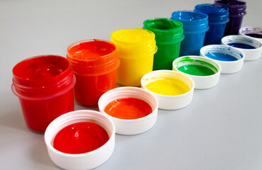 Open cans of paint of different colors stand in a row. Palette, gouache and acrylic paints for creativity, close-up.