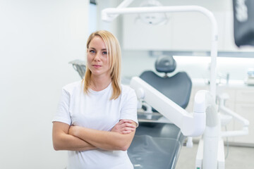 Middle shot of a Caucasian woman wearing a white T-shirt, standing in front of a dental chair at a dental clinic.