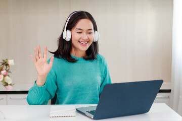 Candid young attractive asian woman student wear earphone studying online course program at home. Asian female adult employee participating on video conference meeting during working from home