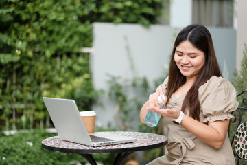 Asian woman using alcohol gel as hand sanitizer antibacterial sanitizer, Workplace desk with a laptop.