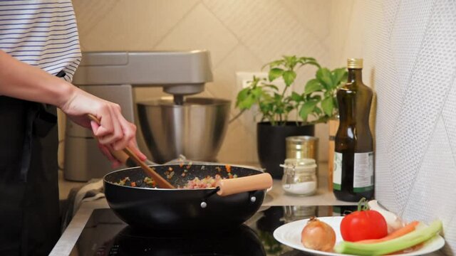 Woman cooking bolognese sauce. Female hand mixing frying ingredient in pan on induction stove