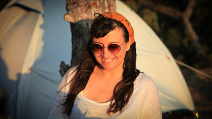 Smiling young woman in front of camping tent at sunset