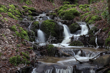 Obraz premium une petite cascade entre rochers et mousse sur un ruisseau en hiver