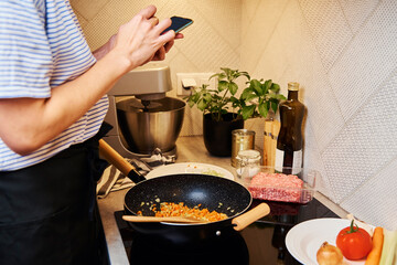 Woman use smartphone while cooking bolognese sauce in pan on induction stove in the kitchen