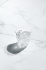 Glass of cold water with ice on sunny marble background, dark shadow. Creative concept