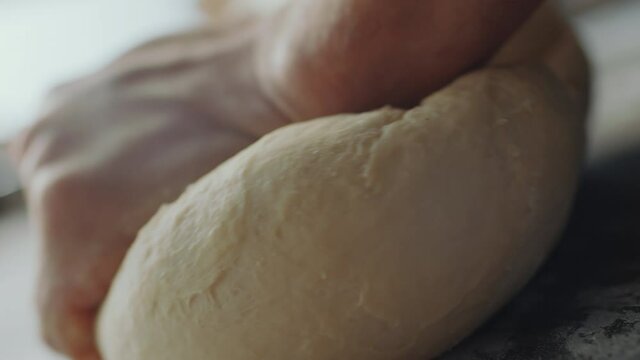 Close up dutch angle shot of hands of baker kneading dough on table