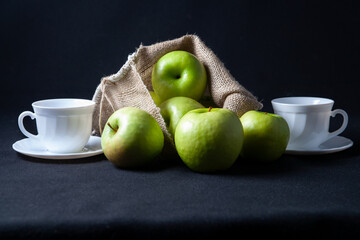 There are green apples on the table. Nearby are two white circles. On a black background.