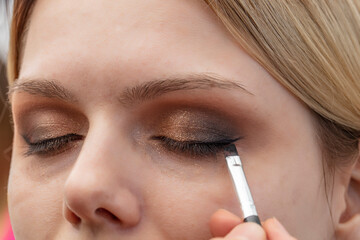 Makeup artist applies eyeshadow. Beautiful woman face. Hand of makeup master, young beauty model girl painting eyes. Makeup in the process