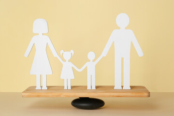 Fototapeta na wymiar Figure of family on teeterboard against yellow background. Concept of balance